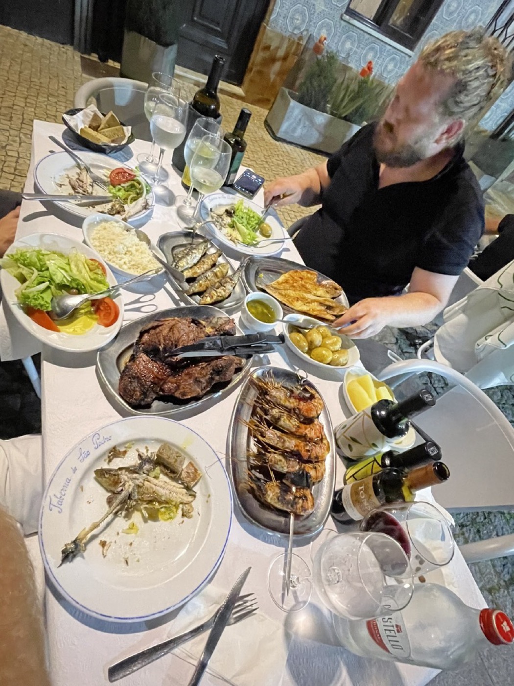 An overhead view of a table on the cobbled street, loaded with grilled fish, rice, salad and olives